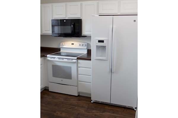 A white refrigerator stands in a kitchen next to a microwave and oven.